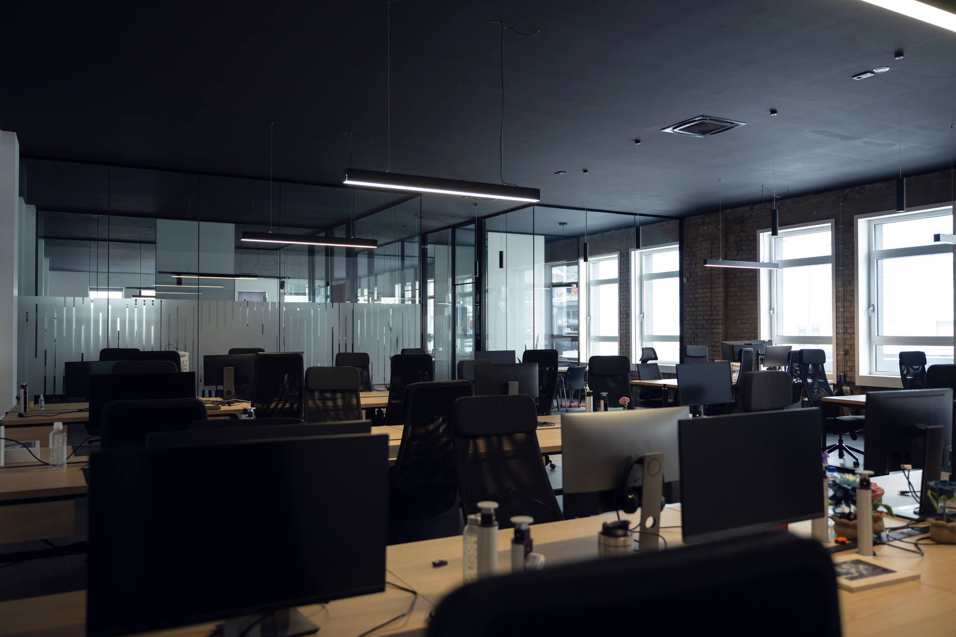 Modern business, glass-walled startup office, open and spacious workspace exudes a modern and innovative vibe, fostering a dynamic atmosphere that supports creativity, collaboration, and business growth. A modern open-plan office with rows of desks, black office chairs, glass partitions, and large windows providing natural light.Retry